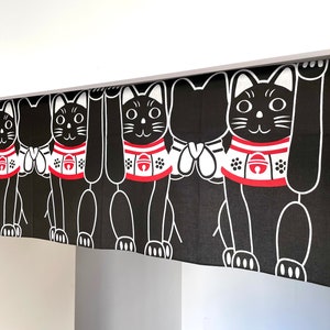 Puede incluir: Cortina Maneki Neko en blanco y negro. El dise&ntilde;o presenta un patr&oacute;n repetido de gatos negros estilizados con patas levantadas, con collares rojos y blancos. Los gatos tienen contornos blancos sobre un fondo negro. La cortina cuelga de una barra blanca.