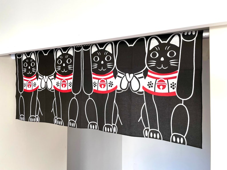 Puede incluir: Cortina Maneki Neko en blanco y negro. El dise&ntilde;o presenta un patr&oacute;n repetido de gatos negros estilizados con patas levantadas, con collares rojos y blancos. Los gatos tienen contornos blancos sobre un fondo negro. La cortina cuelga de una barra blanca.