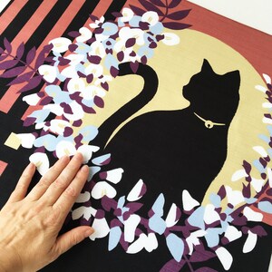 以下が含まれることがあります： 黒猫のシルエットが、金色の首輪をつけて、白と青の藤の花の輪の中に座っています。背景は黒で、右上の角にはピンクと黒のストライプ模様があります。
