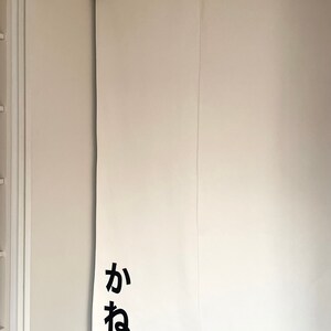 Puede incluir: Puerta corredera blanca con la palabra japonesa "ka" y "ne" escrita en negro en la puerta.