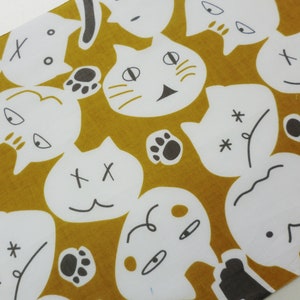 May include: A mustard yellow fabric with a white repeating pattern of cat faces. The cat faces have different expressions, including happy, sad, and surprised. Some of the cat faces have a single X on their foreheads, while others have two Xs. Some of the cat faces have paw prints next to them.