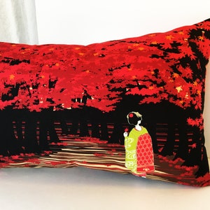 May include: A red and black pillow with a geisha in a green and red kimono walking through a forest of red maple trees. The pillow is rectangular and has a black background with red maple leaves and a geisha in a green and red kimono walking through a forest of red maple trees.