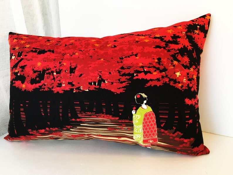 May include: A red and black pillow with a geisha in a green and red kimono walking through a forest of red maple trees. The pillow is rectangular and has a black background with red maple leaves and a geisha in a green and red kimono walking through a forest of red maple trees.