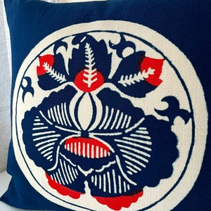 Op de afbeelding: Een blauw kussen met een witte cirkel in het midden. De cirkel heeft een rood en blauw bloemenmotief.