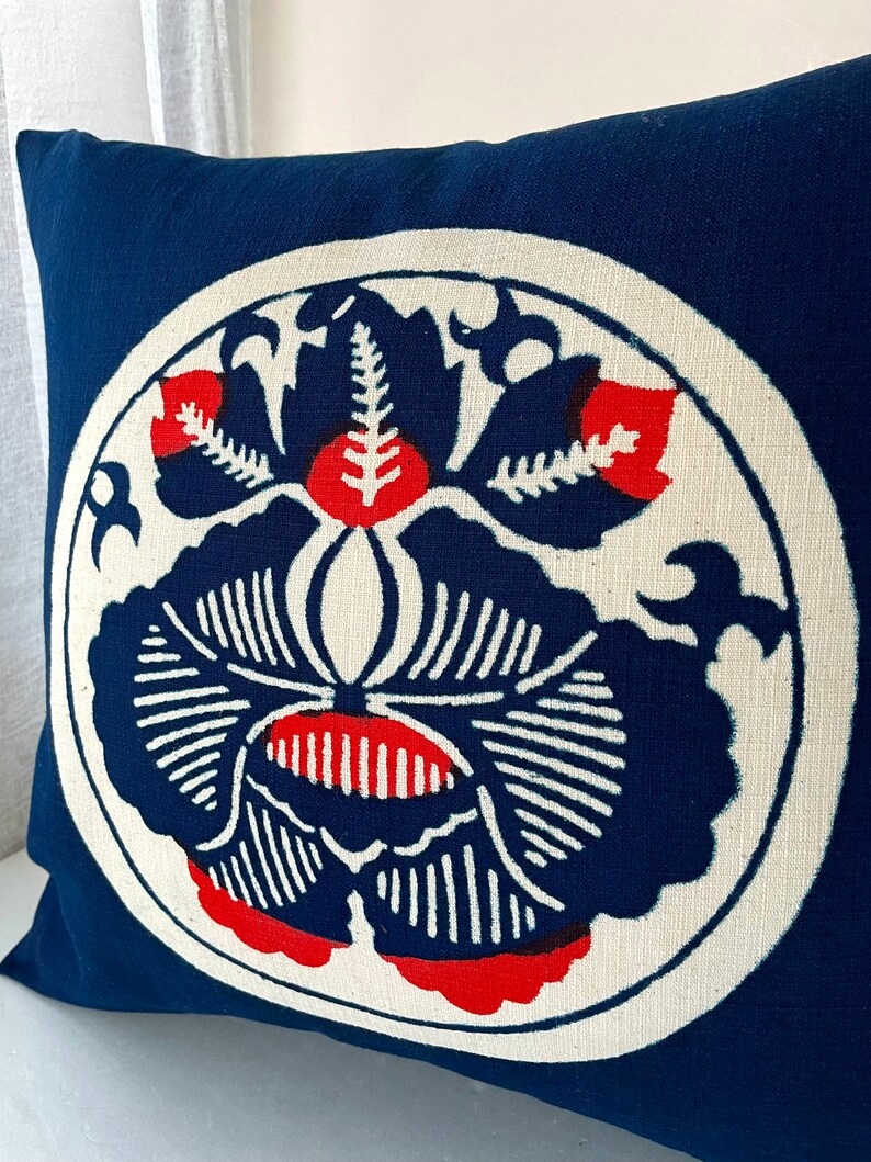 Op de afbeelding: Een blauw kussen met een witte cirkel in het midden. De cirkel heeft een rood en blauw bloemenmotief.