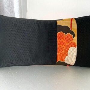 Pode incluir: Travesseiro preto com um painel decorativo de tecido floral laranja, dourado e branco. O travesseiro &eacute; feito de um tecido texturizado.