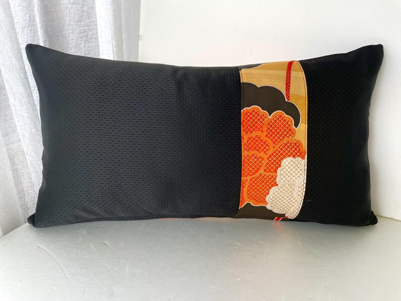 Pode incluir: Travesseiro preto com um painel decorativo de tecido floral laranja, dourado e branco. O travesseiro &eacute; feito de um tecido texturizado.