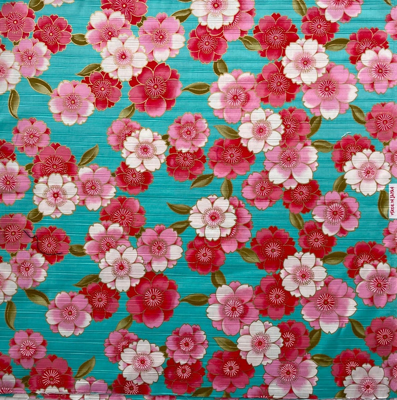 May include: A teal fabric with a repeating pattern of pink and red flowers with gold accents. The flowers have a layered petal design.