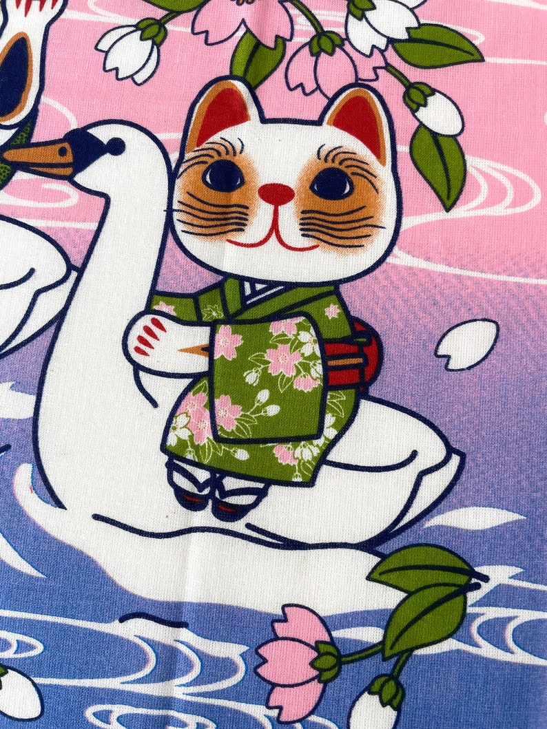 May include: A fabric print featuring a white cat wearing a green floral kimono, riding on the back of a white swan. The background transitions from pink to purple with stylized water ripples and cherry blossom branches with pink flowers.