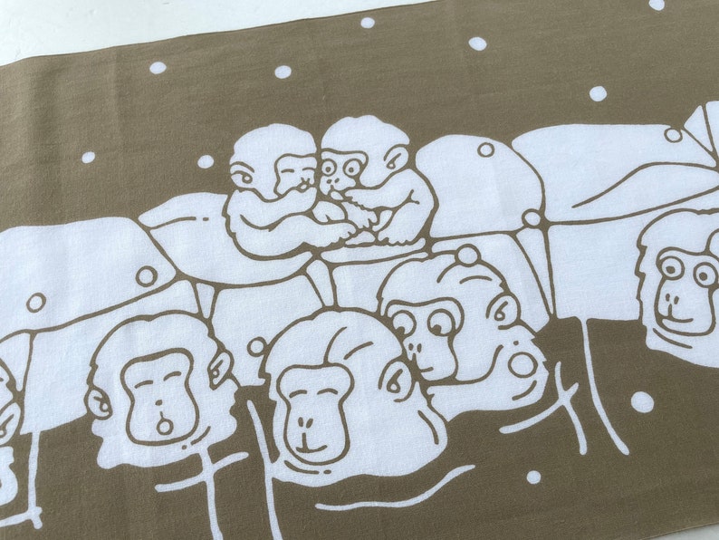 May include: A tan and white textile featuring a repeating pattern of cartoon monkeys. The monkeys are depicted in a simple, line-art style, with some embracing and others with various expressions. White dots are scattered across the tan background.