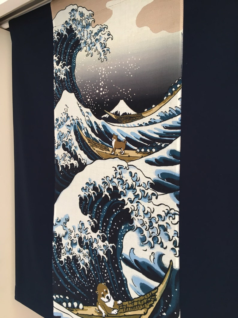May include: A blue and white fabric wall hanging featuring a stylized wave with a dog standing on a boat. The wave is reminiscent of the Great Wave off Kanagawa by Hokusai. The background is a light gray with a mountain in the distance.