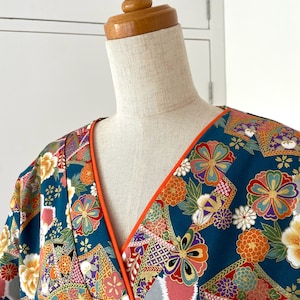 Puede incluir: Un kimono azul turquesa con un estampado floral colorido y ribete naranja alrededor del escote. El kimono est&aacute; en un maniqu&iacute; blanco.