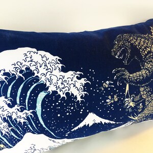 May include: A blue pillow with a white and blue wave design and a Godzilla-like creature in the upper right corner.