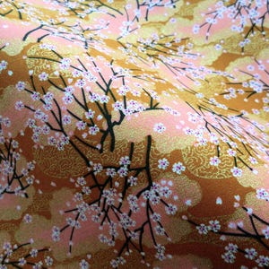 May include: A fabric featuring a pattern of black tree branches with small white and pink cherry blossoms. The background consists of alternating sections of solid light pink and textured metallic gold clouds, creating a layered visual effect.