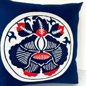 Op de afbeelding: Een blauw kussen met een wit cirkelvormig ontwerp met een rood en zwart bloemenpatroon.