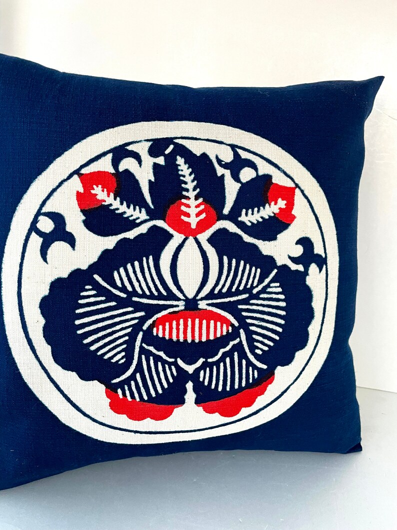 Op de afbeelding: Een blauw kussen met een wit cirkelvormig ontwerp met een rood en zwart bloemenpatroon.