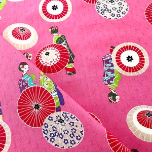 May include: Pink fabric with a repeating pattern of geishas and red and white umbrellas. The umbrellas have a white background with red spokes and a black center.