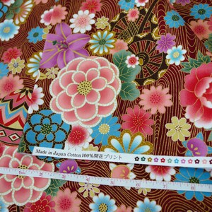 May include: A dark red cotton fabric featuring a floral pattern with pink, blue, and purple flowers, and gold line details. A white measuring tape shows a length of 10 inches. The fabric edge includes the text Made in Japan Cotton 100% and flower icons.
