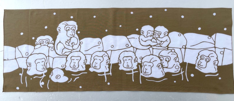 May include: A brown rectangular towel featuring a white illustration of several monkeys. The monkeys are depicted in a hot spring, with some holding babies. White dots are scattered across the background.