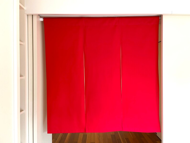 May include: Three panels of red fabric hang from a white rod. The fabric is smooth and has a slight sheen. The panels are evenly spaced and hang straight down.