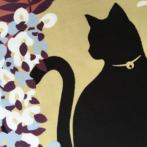以下が含まれることがあります： 金色の首輪をした黒い猫のシルエットで、尻尾が体の周りに巻き付いている。猫は、白、紫、青の色合いの花柄の黄色い背景の上にいる。
