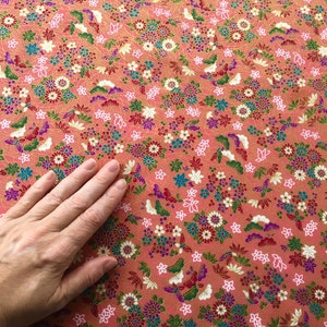 May include: A close-up of a pink fabric with a floral pattern. The fabric is covered in small, colorful flowers and butterflies. The fabric is smooth and soft.