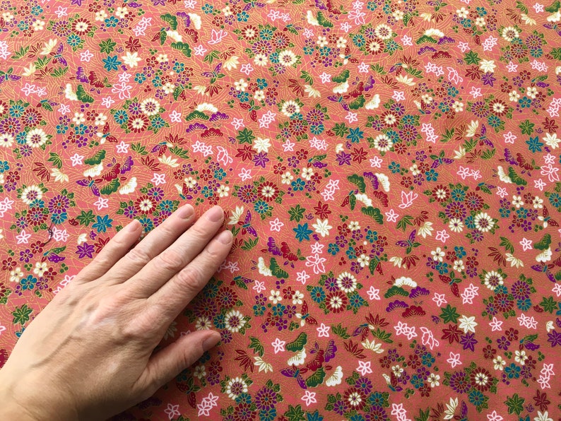 May include: A close-up of a pink fabric with a floral pattern. The fabric is covered in small, colorful flowers and butterflies. The fabric is smooth and soft.