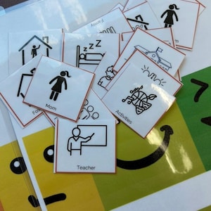 May include: A collection of square white laminated cards with black line art icons and text labels. Visible labels include Mom, Teacher, and Activities. The icons depict various daily life symbols such as a person at a chalkboard, a house, and sports equipment, all arranged in a scattered pile.