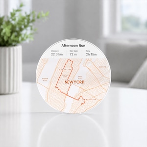 May include: A circular white plaque featuring an orange map of New York City with a highlighted running route. The text reads Afternoon Run, Distance 22.3 km, Elev Gain 72 m, Time 2h 15m, Manhattan, Central Park, Queens, Hudson River, East River, Brooklyn, and NEWYORK.