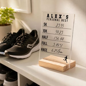May include: A clear acrylic plaque with a wooden base displaying the text ALEX'S PERSONAL BEST and a list of running times for 5K, 10K, HALF, FULL, and RACE, accompanied by a small black silhouette of a runner at the bottom right corner.