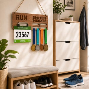 May include: A rectangular wooden wall-mounted display board with a rope hanger, featuring the engraved text RUN. and SMITH'S MEDALS. It includes a metal clip holding a race bib numbered 23567 and four slots for hanging medals with blue, teal, orange, and green ribbons.