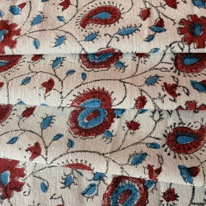 Può includere: Un tessuto intrecciato con un motivo ripetuto di fiori rosso scuro e forme paisley blu su uno sfondo bianco sporco. Il design presenta sottili steli scuri e sinuosi che collegano i motivi floreali e paisley su tutta la superficie.