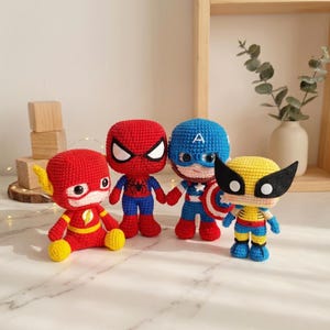 Puede incluir: Cuatro muñecos de ganchillo hechos a mano que representan superhéroes. Las figuras incluyen a Flash en rojo y amarillo, Spider-Man en rojo y azul, Capitán América en azul y blanco con escudo, y Wolverine en amarillo y azul con máscara negra.