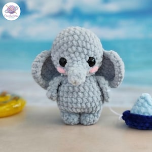 Puede incluir: Un pequeño peluche de elefante tejido a ganchillo en color gris claro con orejas grandes, ojos de seguridad negros y mejillas bordadas en rosa. El elefante tiene una textura de hilo suave y está de pie con cabeza y trompa redondeadas.