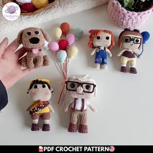 Puede incluir: Una colección de seis muñecos de ganchillo hechos a mano inspirados en la película Up, que incluye un anciano con gafas, un joven explorador, dos figuras femeninas, un perro marrón y un racimo de pequeños globos de lana con hilos blancos.