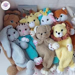 Puede incluir: Una colección de peluches hechos de hilo suave, que incluye un conejo gris, un gato marrón, una jirafa amarilla, un unicornio blanco con crines coloridas, un perro marrón, un león con melena marrón y un zorro, todos con detalles bordados.
