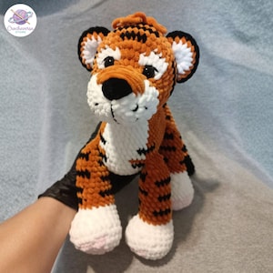 Puede incluir: Un juguete de tigre de peluche hecho de hilo suave naranja, negro y blanco. El animal de peluche presenta una cabeza redondeada con orejas de punta negra, ojos oscuros, una nariz negra y un hocico blanco. Su cuerpo tiene rayas negras.
