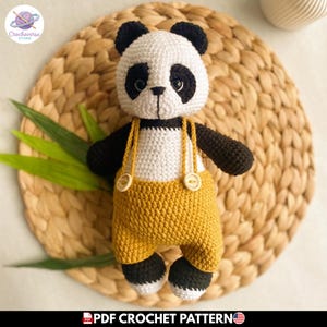 Puede incluir: Un juguete de panda tejido a ganchillo hecho a mano con cabeza blanca y negra, parches oscuros en los ojos, brazos negros y pies blancos. El panda lleva un peto amarillo mostaza con dos botones claros en los tirantes. Texto PDF CROCHET PATTERN visible.