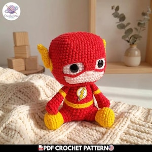 Puede incluir: Una muñeca de ganchillo roja y amarilla con una máscara de ojos negros, una sección inferior de la cara blanca, detalles de rayos amarillos en las orejas y un emblema de rayo amarillo en el pecho. El texto PDF CROCHET PATTERN es visible abajo.