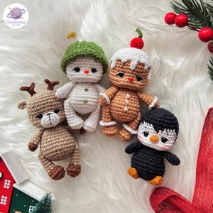 Puede incluir: Cuatro pequeños peluches de ganchillo que incluyen un reno beige con astas, un muñeco de nieve blanco con un gorro verde, una figura de pan de jengibre marrón con glaseado blanco y una cereza roja, y un pingüino blanco y negro.