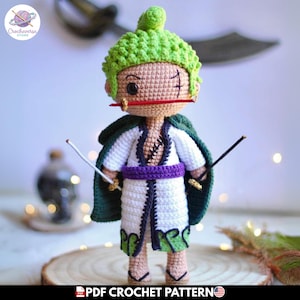 Puede incluir: Una muñeca amigurumi tejida a ganchillo a mano que representa un personaje con cabello corto verde lima, tez bronceada y una cicatriz sobre un ojo. Viste una túnica blanca con bordes oscuros, una faja morada y una capa verde oscuro.
