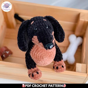 Puede incluir: Un juguete de peluche de perro salchicha hecho de hilo negro y bronceado con una nariz negra lisa y ojos oscuros. El juguete presenta orejas largas y caídas y una superficie texturizada. El texto PDF CROCHET PATTERN es visible en la parte inferior.