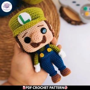 Puede incluir: Muñeco de ganchillo hecho a mano de un personaje con un gorro verde con una "L" blanca, un bigote marrón y un peto azul. El muñeco tiene ojos de botón negros y pelo castaño. El texto "PDF CROCHET PATTERN" está en la parte inferior.