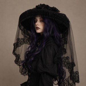 Puede incluir: Un sombrero negro de ala ancha con una copa adornada con flores de tela, un borde decorado con cuentas negras colgantes y un largo velo de encaje negro transparente con intrincados bordados florales sobre los hombros.