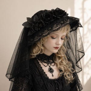 Puede incluir: Sombrero negro de ala ancha, adornado con rosas y hojas negras. El sombrero presenta un delicado ribete de encaje y se combina con un velo negro. El diseño es gótico y elegante.