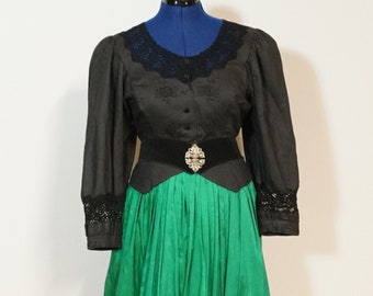 May include: A traditional black and green dress with a fitted bodice and a full skirt. The bodice features a black lace collar and long sleeves. The skirt is a vibrant green with black trim. A black belt with a decorative buckle cinches the waist.