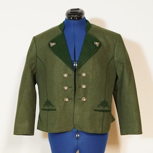 Puede incluir: Una chaqueta de lana verde con cuello de terciopelo verde oscuro y botones decorativos. La chaqueta tiene detalles bordados en la parte delantera y los bolsillos.