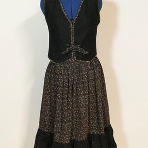 Könnte beinhalten: Ein Vintage-Kleid und Weste Set. Die schwarze Weste hat einen V-Ausschnitt und eine Schleife. Der Rock hat einen Blumendruck mit einem schwarzen Polka-Dot-Saum. Das Kleid wird auf einer blauen Schaufensterpuppe präsentiert.