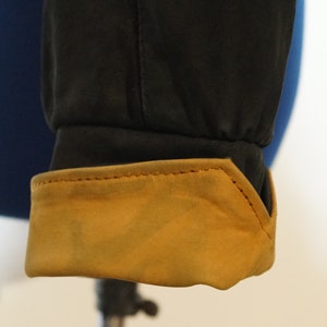May include: Close-up of a black jacket cuff with a brown suede lining. The cuff has a stitched seam around the edge.