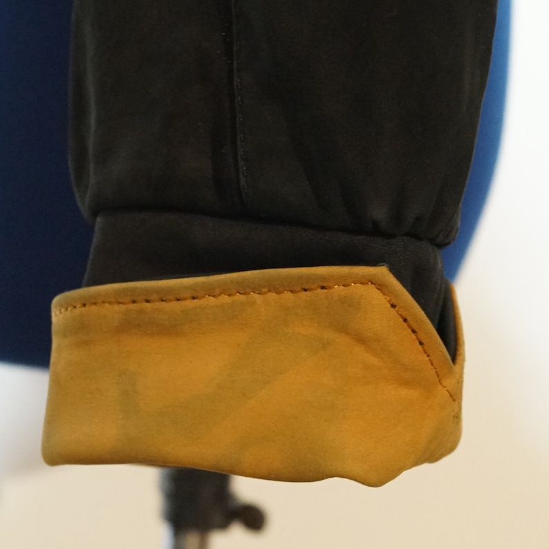 May include: Close-up of a black jacket cuff with a brown suede lining. The cuff has a stitched seam around the edge.